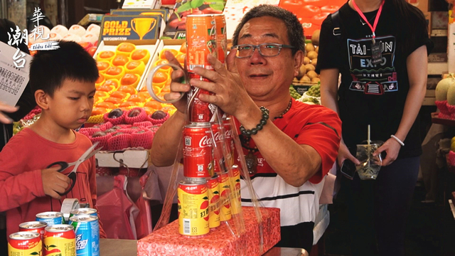 店家周秋安示範堆疊罐頭塔技巧，孫子在一旁協助教學